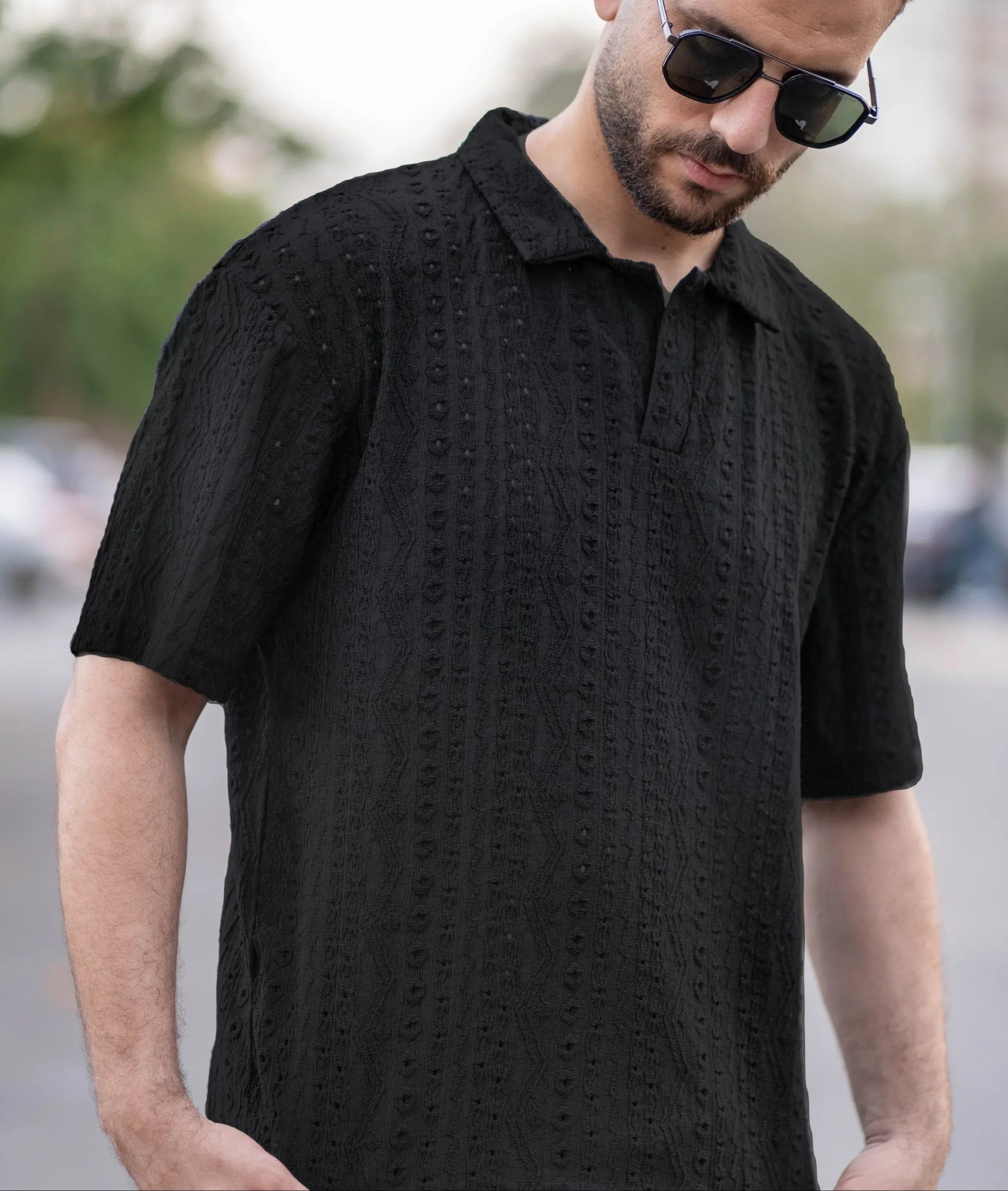 Man wearing a black patterned shirt and sunglasses outdoors