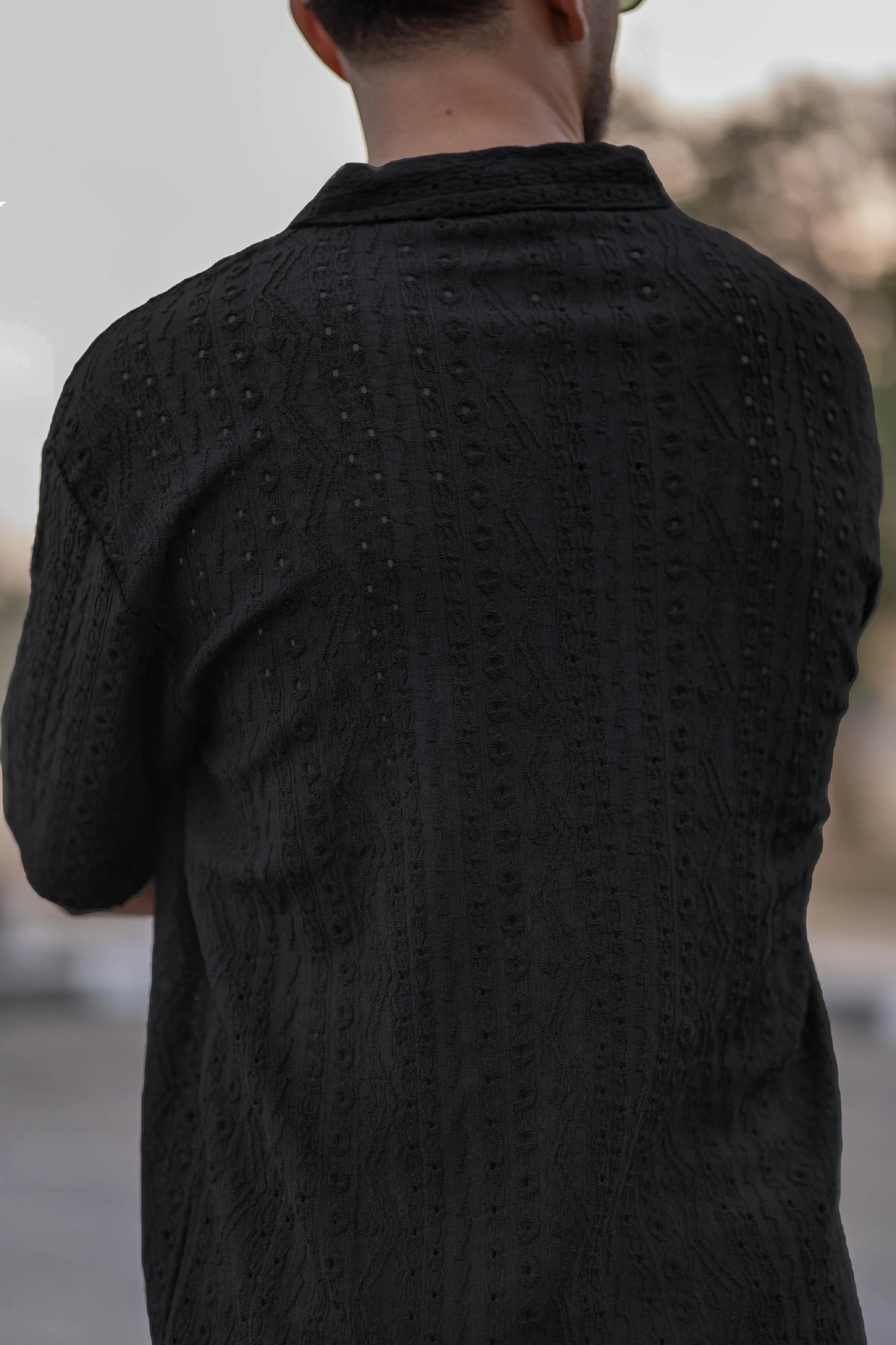 Person wearing a textured black shirt with a blurred background