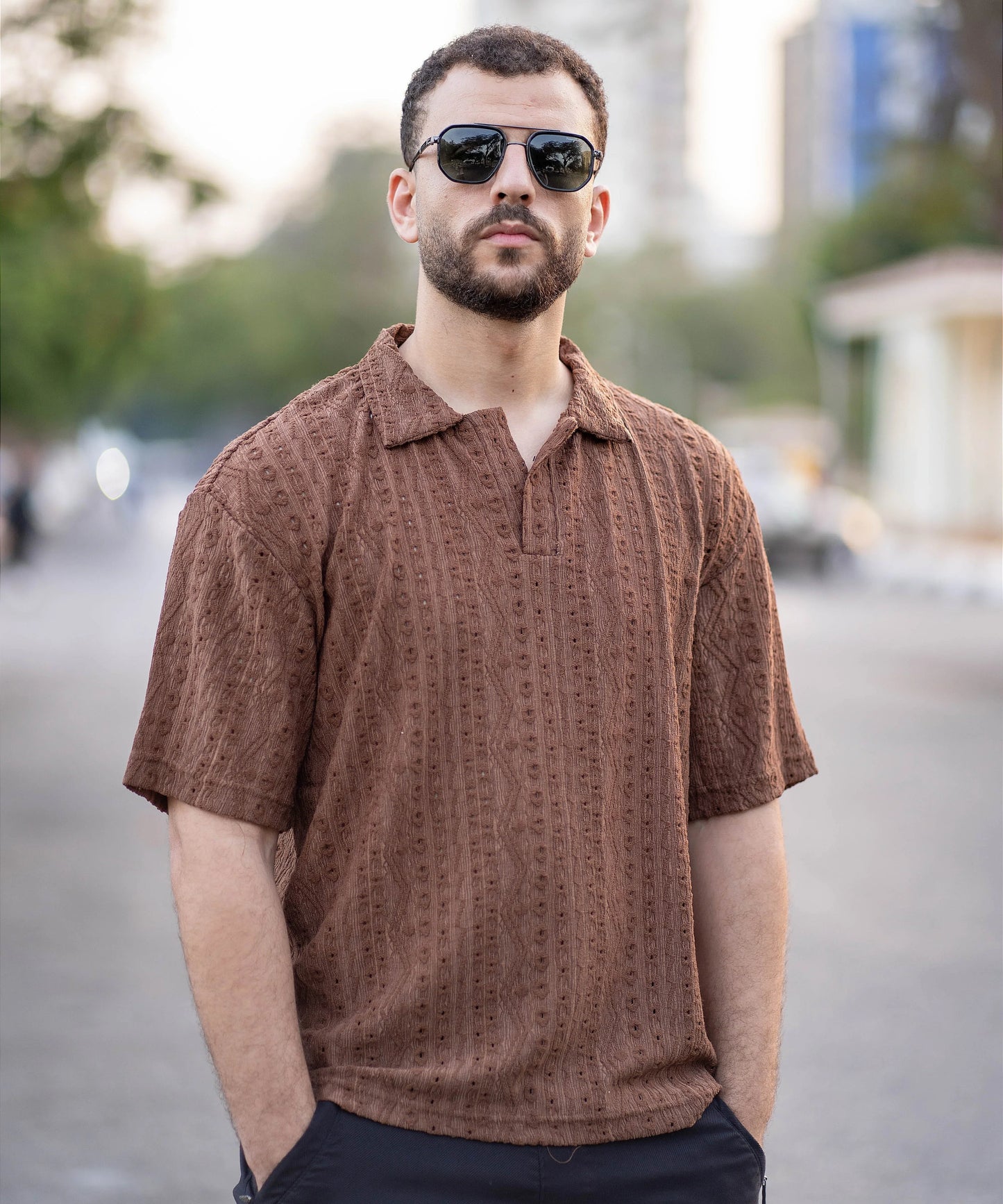 Man wearing a brown patterned shirt and sunglasses on a blurred street background