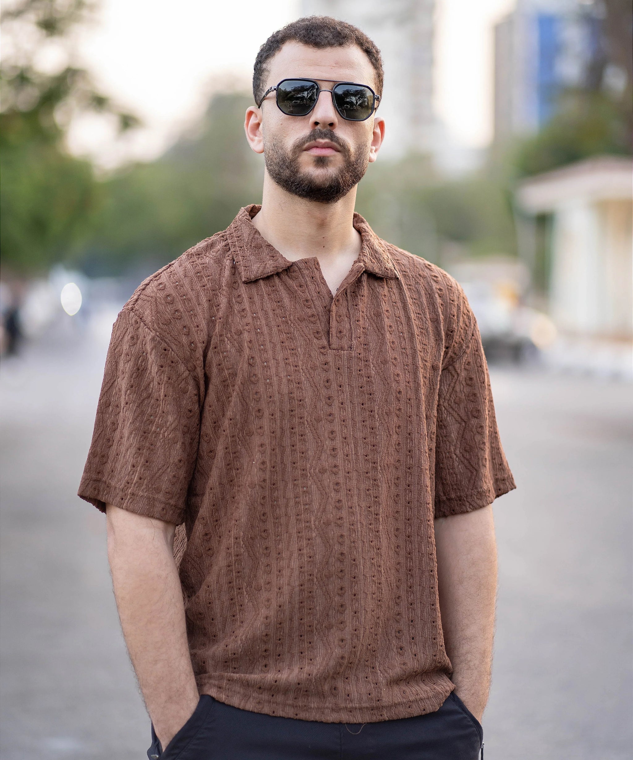 Man wearing a brown patterned shirt and sunglasses on a blurred street background