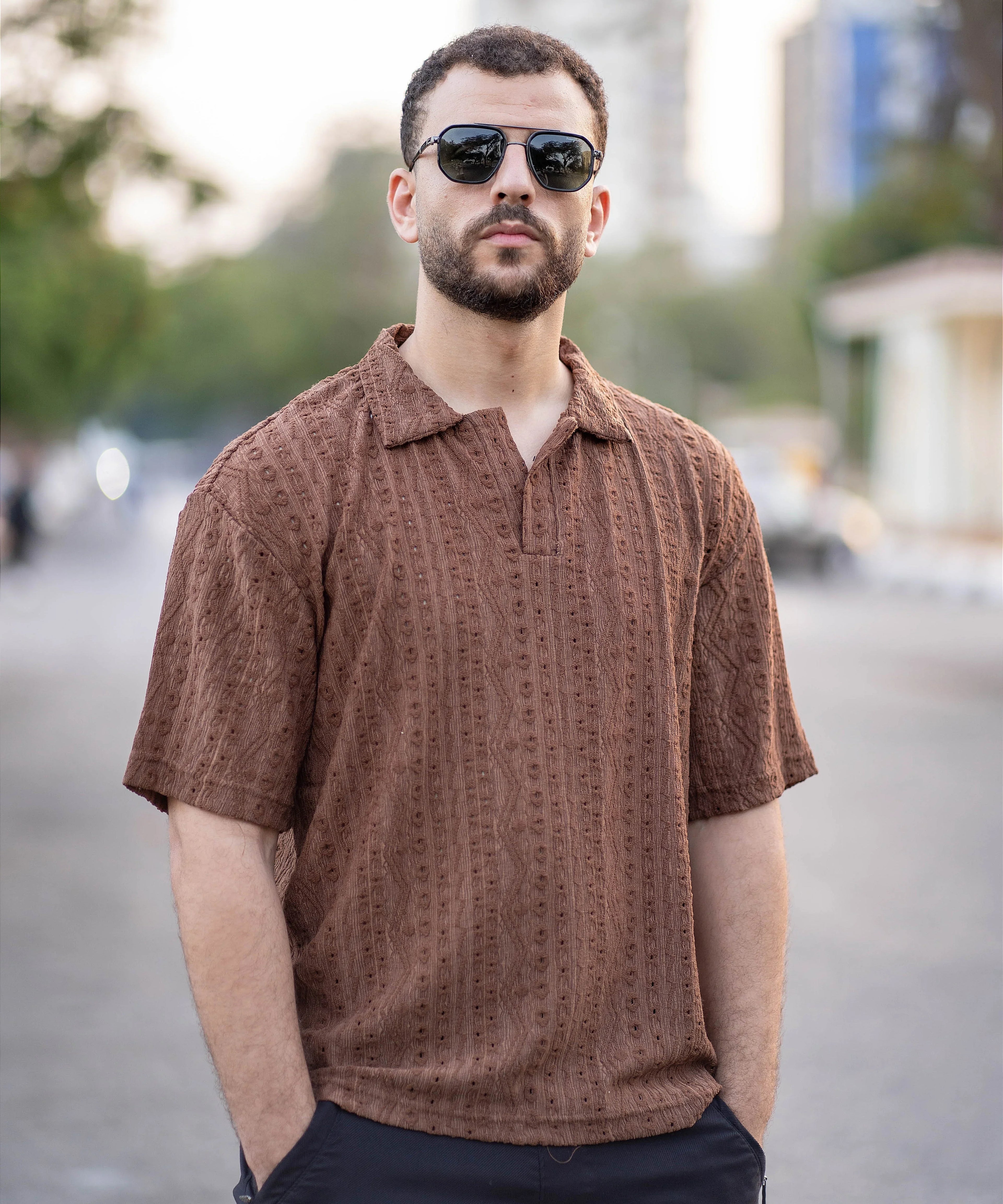 Man wearing a brown patterned shirt and sunglasses on a blurred street background