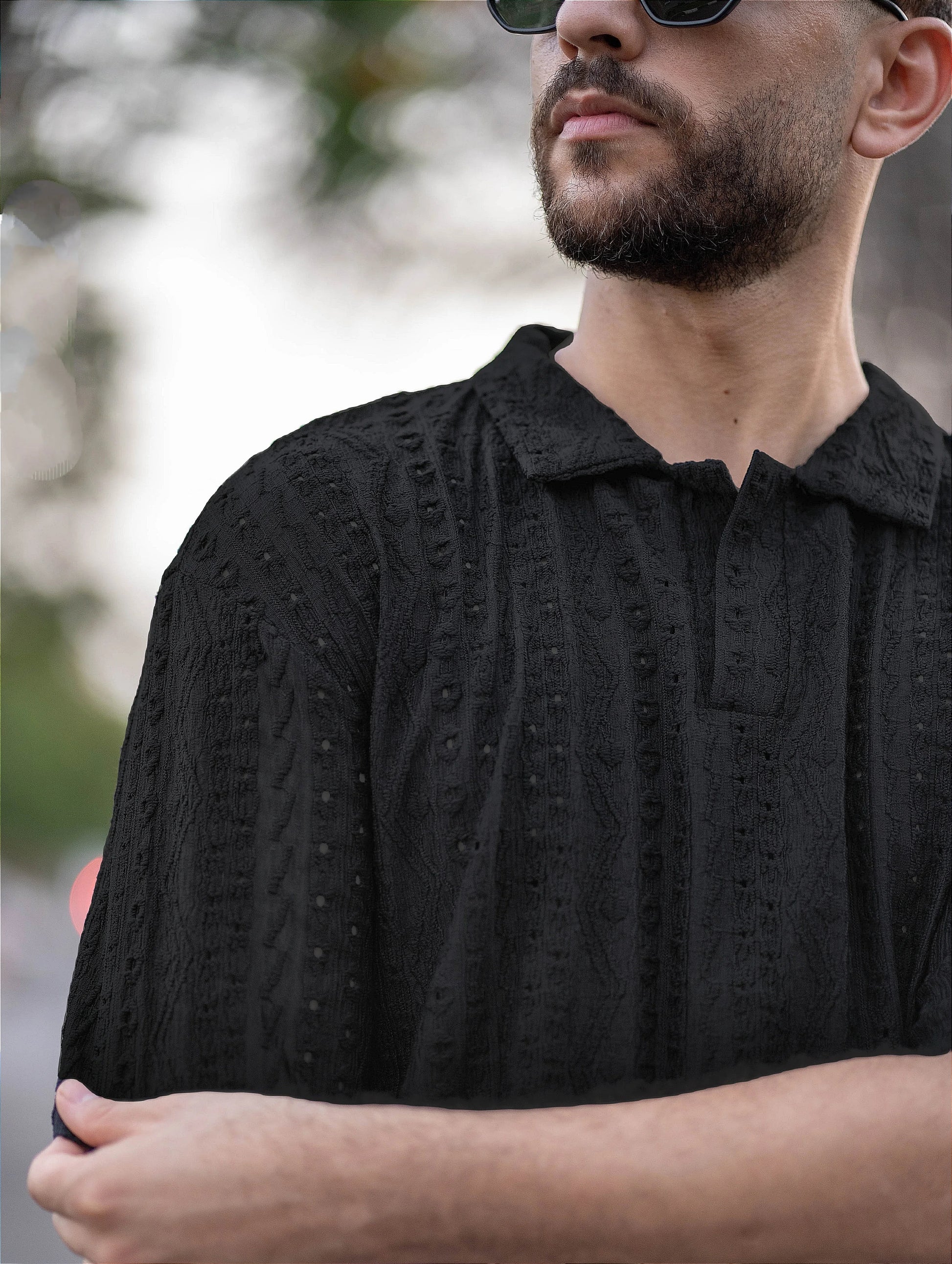 Man wearing a black embroidered shirt with a blurred background