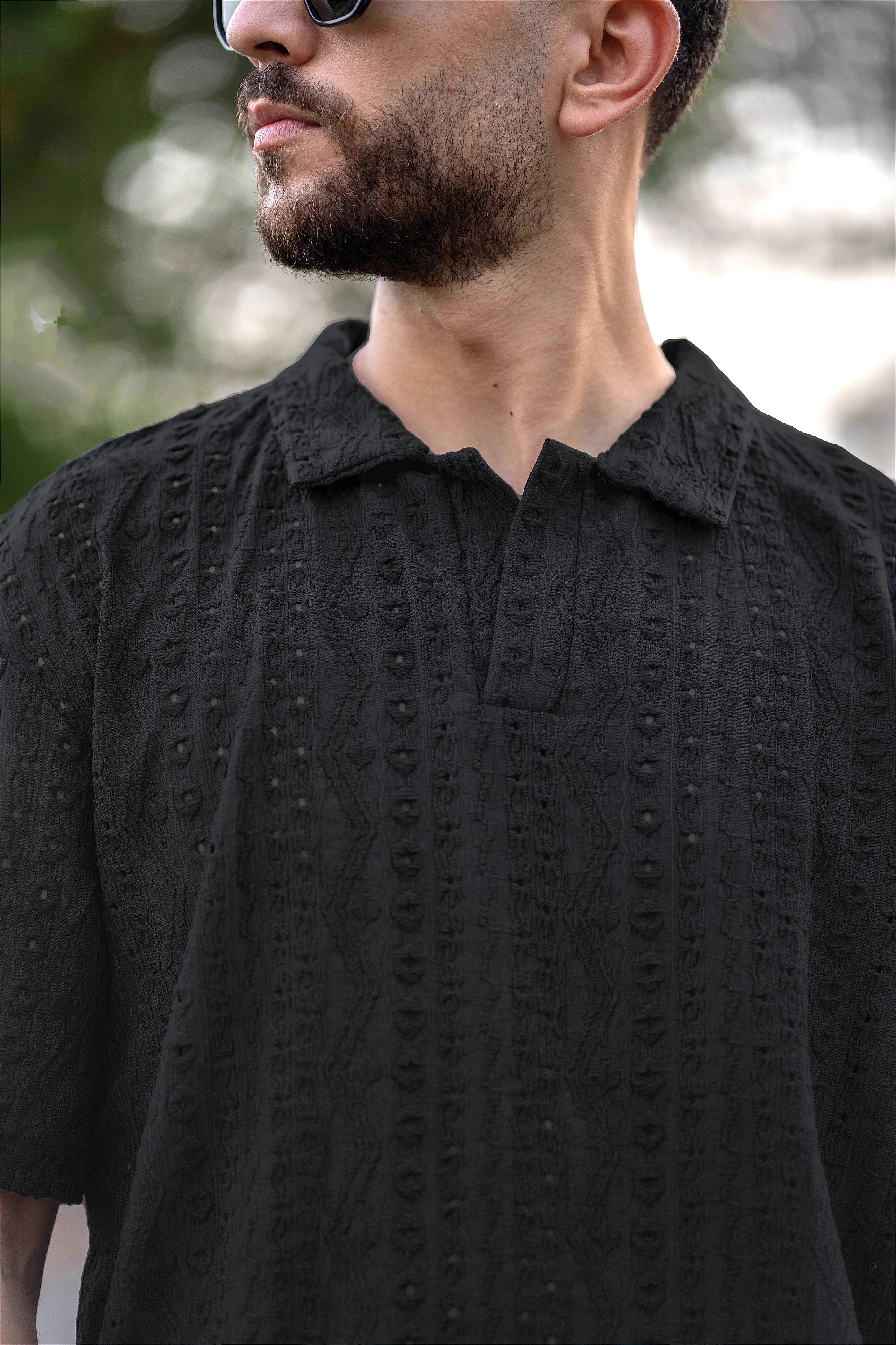 Man wearing a black textured shirt with a blurred background